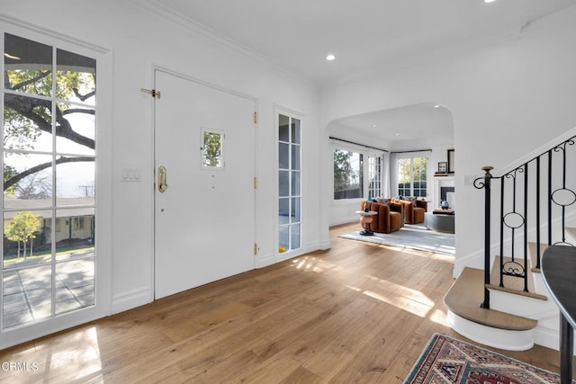 entrance foyer featuring ornamental molding, stairway, light wood-style floors, a fireplace, and recessed lighting