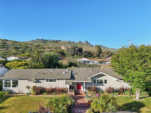 single story home with board and batten siding, a mountain view, a shingled roof, and a front lawn