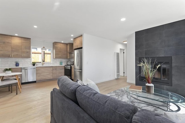 living room featuring recessed lighting, a tile fireplace, light wood-type flooring, and baseboards