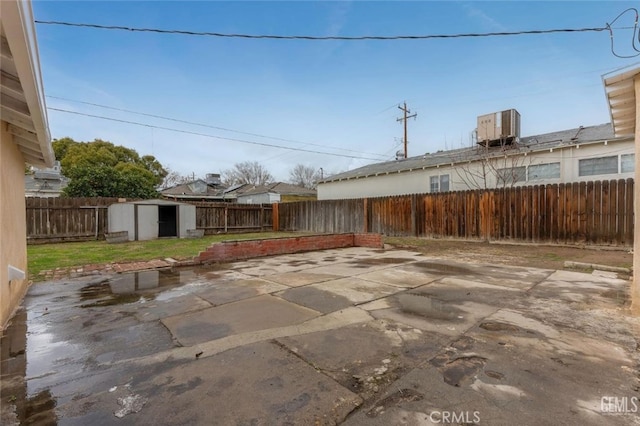 view of patio with an outbuilding, a storage shed, cooling unit, and a fenced backyard