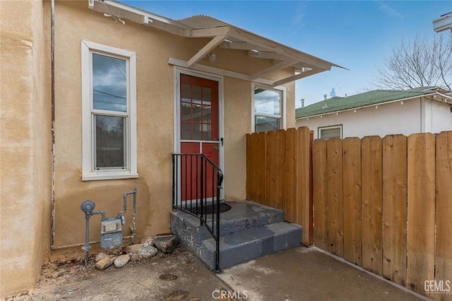 doorway to property featuring fence and stucco siding