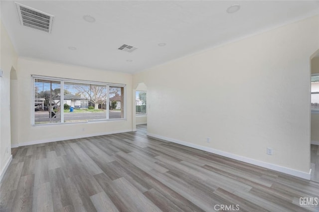 spare room featuring light wood-style floors, visible vents, arched walkways, and baseboards