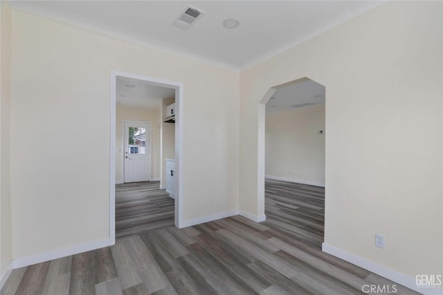 unfurnished room with baseboards, visible vents, arched walkways, and wood finished floors