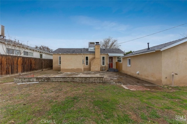 back of house featuring a lawn, a fenced backyard, a chimney, a patio area, and stucco siding