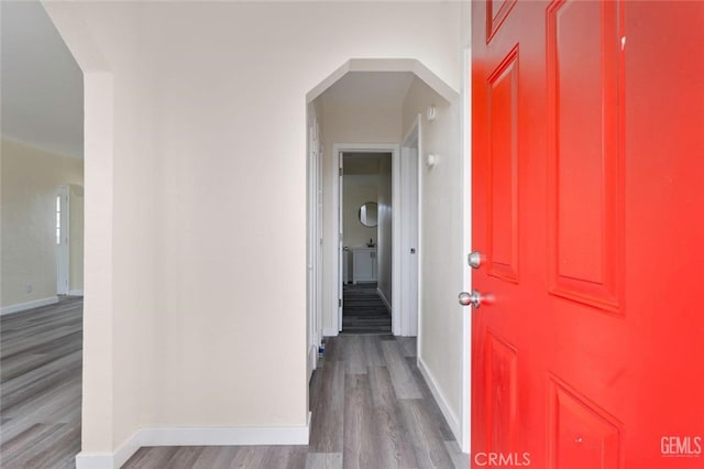 hallway featuring light wood-style floors, baseboards, and arched walkways