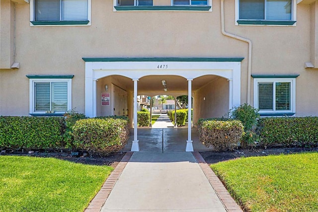 view of exterior entry featuring a lawn and stucco siding