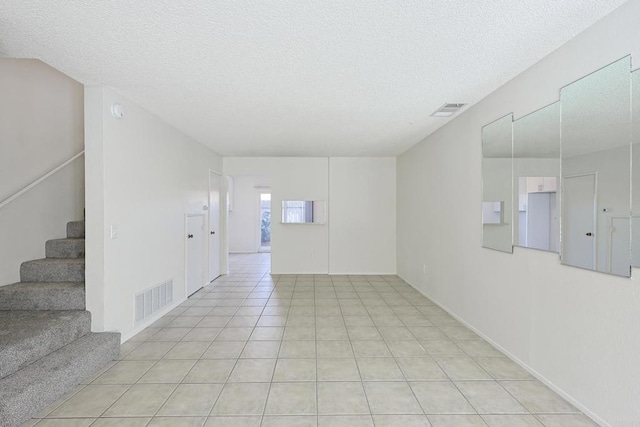 empty room featuring light tile patterned floors, stairway, a textured ceiling, and visible vents