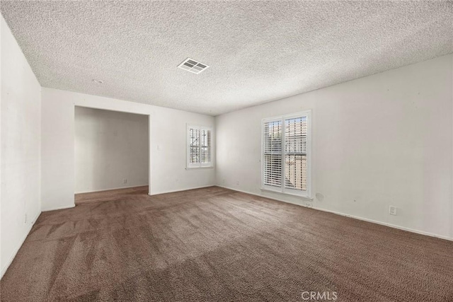 spare room with a textured ceiling, visible vents, and carpet flooring