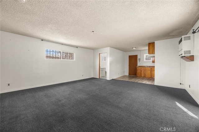 unfurnished living room featuring a textured ceiling, carpet floors, and baseboards