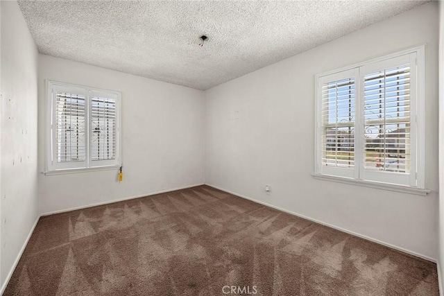 spare room with plenty of natural light, a textured ceiling, and dark carpet