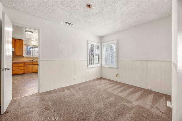 spare room featuring light colored carpet, a wainscoted wall, visible vents, and plenty of natural light