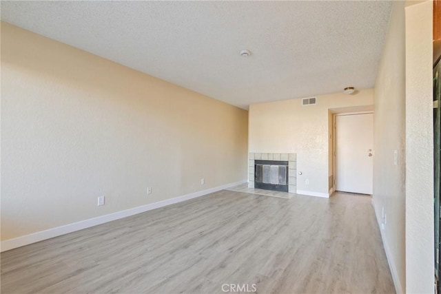 unfurnished living room with a fireplace, visible vents, light wood-style floors, a textured ceiling, and baseboards