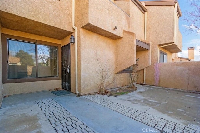 view of exterior entry featuring a patio area, fence, and stucco siding