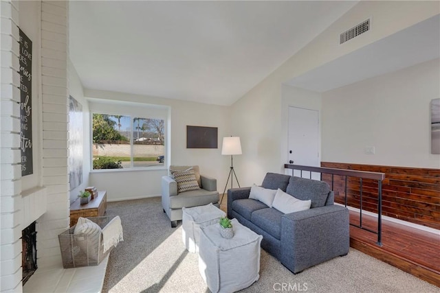 living area featuring baseboards, visible vents, light colored carpet, lofted ceiling, and a brick fireplace