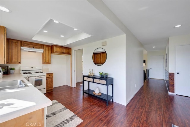 kitchen with under cabinet range hood, white range with gas stovetop, light countertops, dark wood-style floors, and a tray ceiling