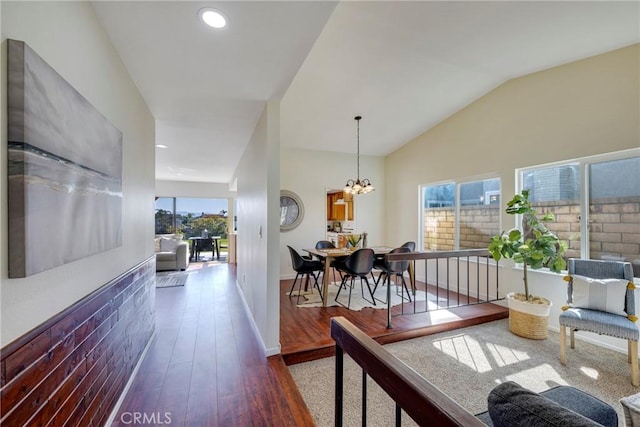 hallway featuring baseboards, lofted ceiling, wood finished floors, a notable chandelier, and recessed lighting