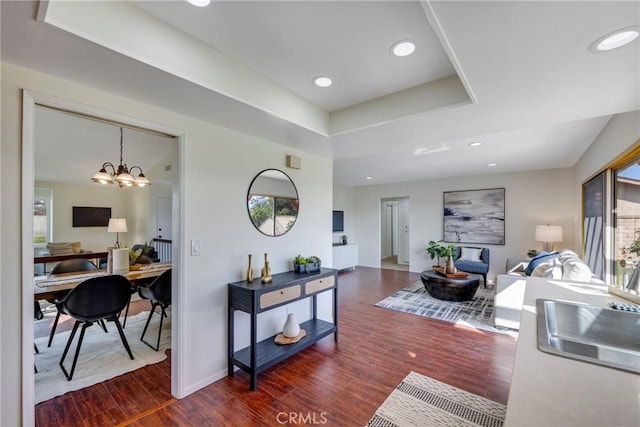 interior space featuring baseboards, a raised ceiling, dark wood-style flooring, an inviting chandelier, and recessed lighting