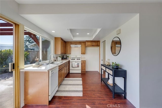 kitchen with a tray ceiling, brown cabinets, light countertops, a sink, and white appliances