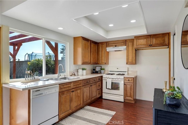 kitchen featuring a tray ceiling, light countertops, a sink, white appliances, and under cabinet range hood