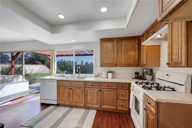 kitchen with white appliances, a sink, dark wood finished floors, light countertops, and a raised ceiling