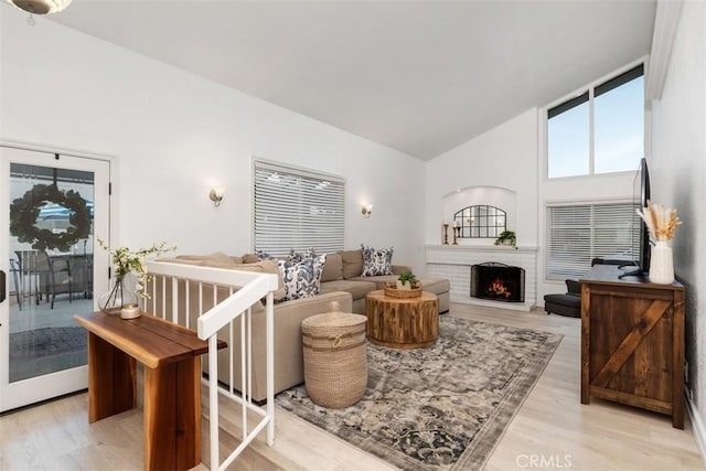 living area featuring a brick fireplace, high vaulted ceiling, and light wood-style floors