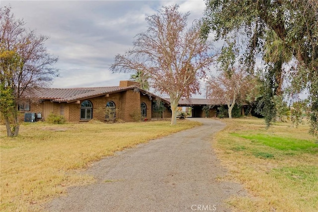 ranch-style home with driveway, a chimney, an attached carport, cooling unit, and a front lawn