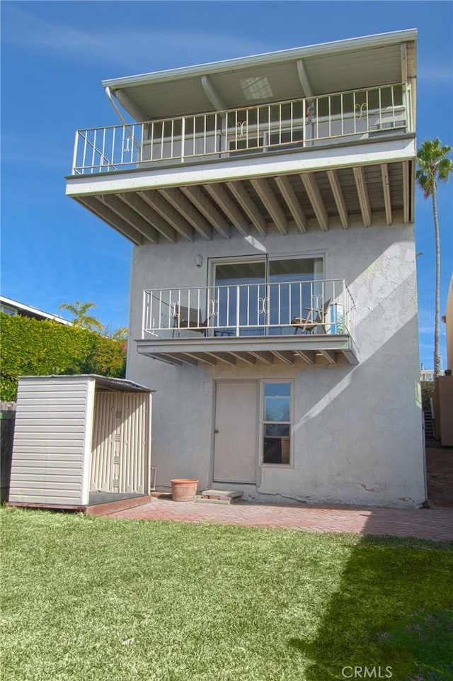 rear view of property featuring a yard, a balcony, and stucco siding