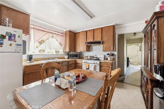 kitchen with brown cabinets, light countertops, a sink, white appliances, and under cabinet range hood