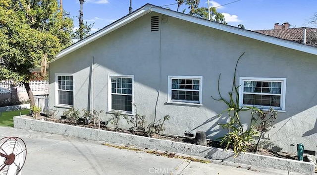 view of side of property with a chimney, a patio area, fence, and stucco siding