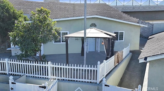 exterior space with roof with shingles, fence, a gazebo, and stucco siding