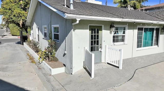 property entrance with roof with shingles and stucco siding