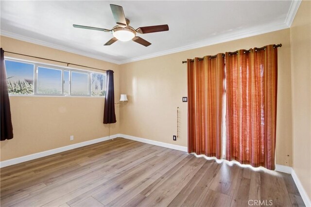 spare room featuring ornamental molding, light wood-type flooring, baseboards, and a ceiling fan