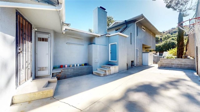 rear view of house with entry steps, a chimney, a patio area, and stucco siding