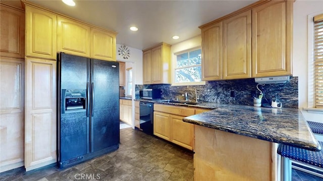 kitchen with a peninsula, a sink, backsplash, black appliances, and dark stone countertops