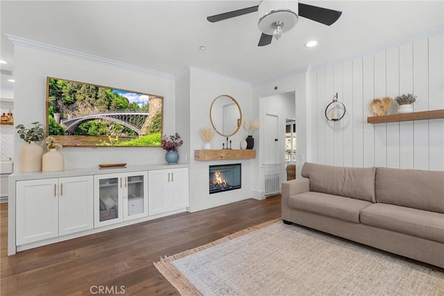 living area featuring ceiling fan, a warm lit fireplace, recessed lighting, dark wood-style floors, and crown molding