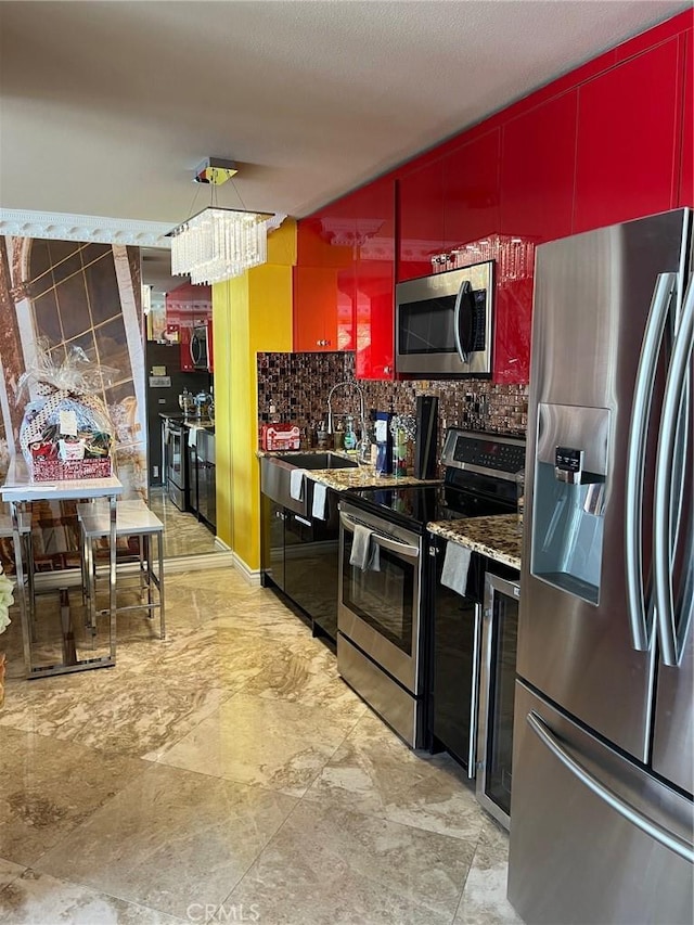 kitchen with red cabinetry, modern cabinets, appliances with stainless steel finishes, backsplash, and a notable chandelier