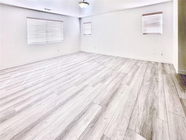 empty room featuring visible vents, wood finished floors, and baseboards