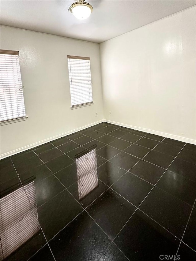 empty room with dark tile patterned flooring and baseboards