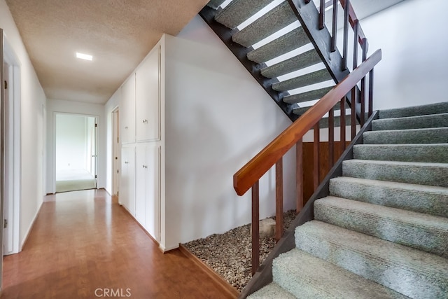 stairs with a textured ceiling and wood finished floors