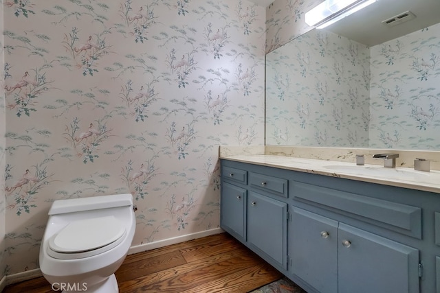 bathroom with toilet, wallpapered walls, visible vents, and wood finished floors