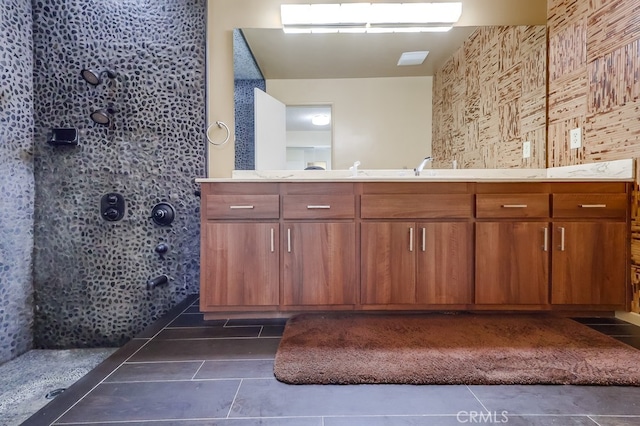 bathroom with tile patterned floors, tiled shower, a sink, and double vanity