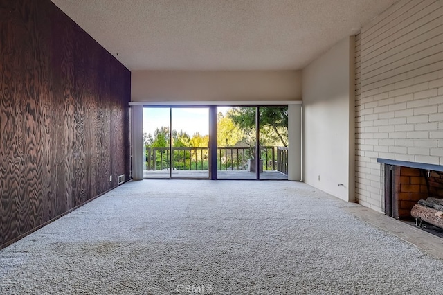 unfurnished living room featuring light carpet, a brick fireplace, wooden walls, and a textured ceiling