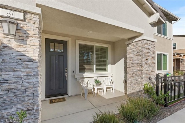 property entrance with stone siding, fence, and stucco siding