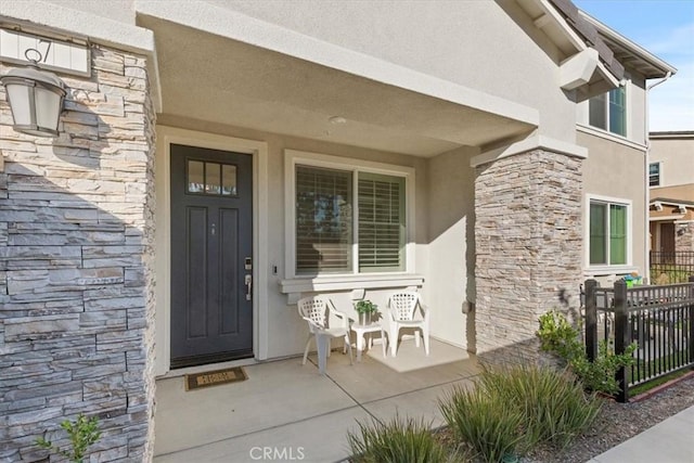 entrance to property with a porch, fence, stone siding, and stucco siding