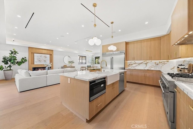 kitchen with premium appliances, an island with sink, open floor plan, light stone countertops, and premium range hood