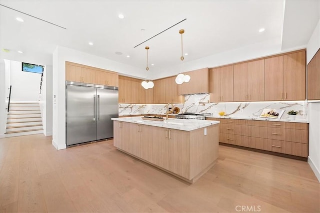 kitchen with light stone countertops, light wood-style flooring, an island with sink, modern cabinets, and built in refrigerator