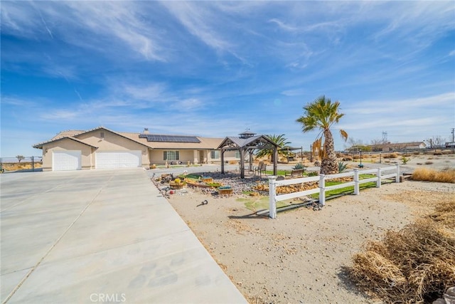 view of front of home featuring stucco siding, fence, concrete driveway, an attached garage, and solar panels