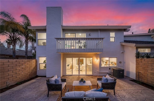 back of house at dusk with a chimney, stucco siding, a patio area, a balcony, and cooling unit