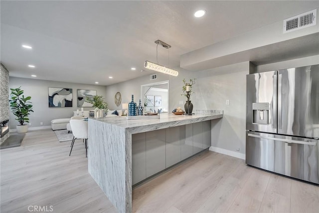 kitchen with visible vents, modern cabinets, a peninsula, light wood-style floors, and stainless steel refrigerator with ice dispenser