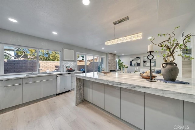 kitchen featuring gray cabinetry, a sink, light stone countertops, dishwasher, and light wood finished floors